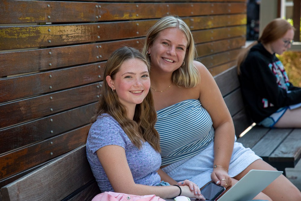 Two smiling students sitting outside on lawn at UC Blue Ash College