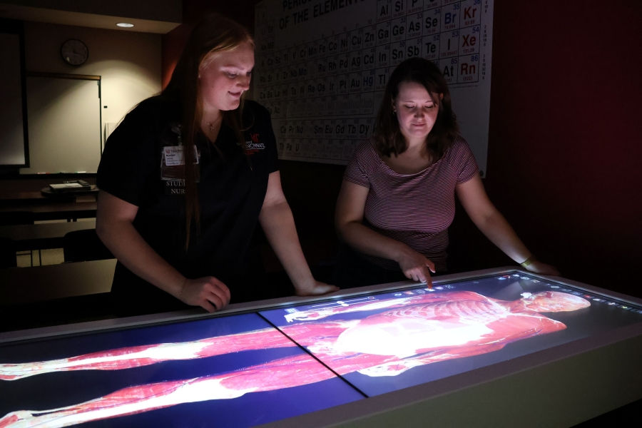 two lab technicians looking at a human body scan on anatomage table