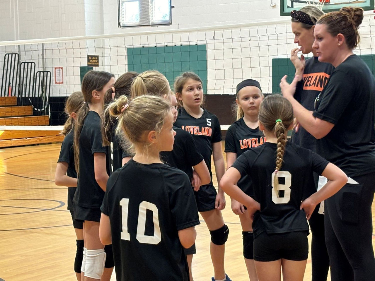 elemtary girls volleyball team in gym with two coaches