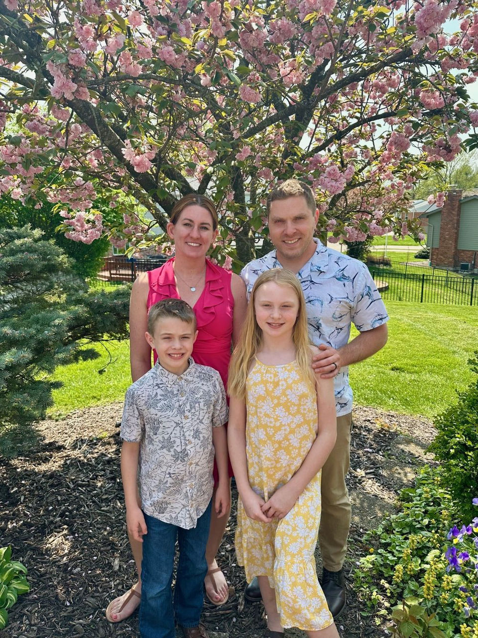 family of four posing together in front of a tree