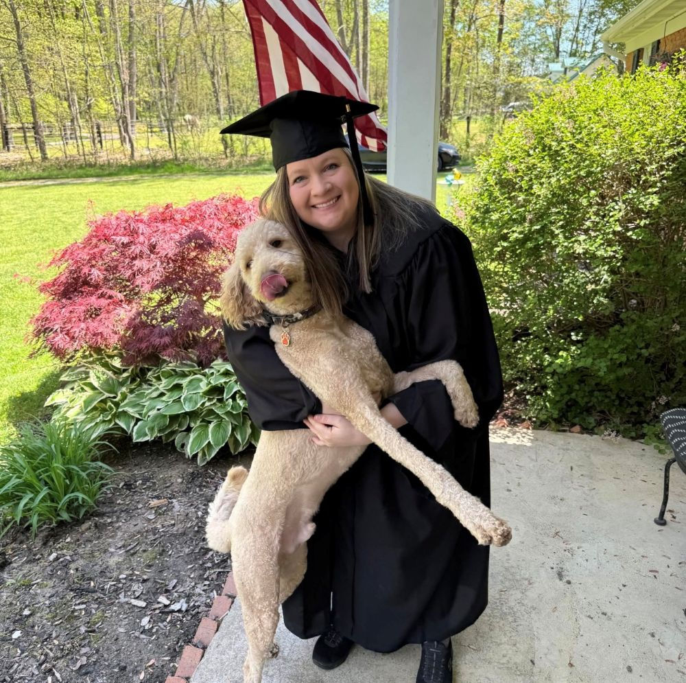 woman in graduation cap and gown with dog on front porch