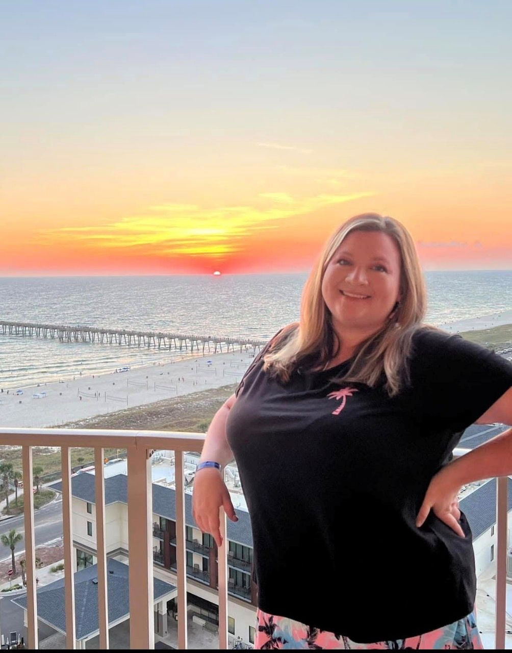 woman smiling and standing on a balcony in front of a sunset over the ocean