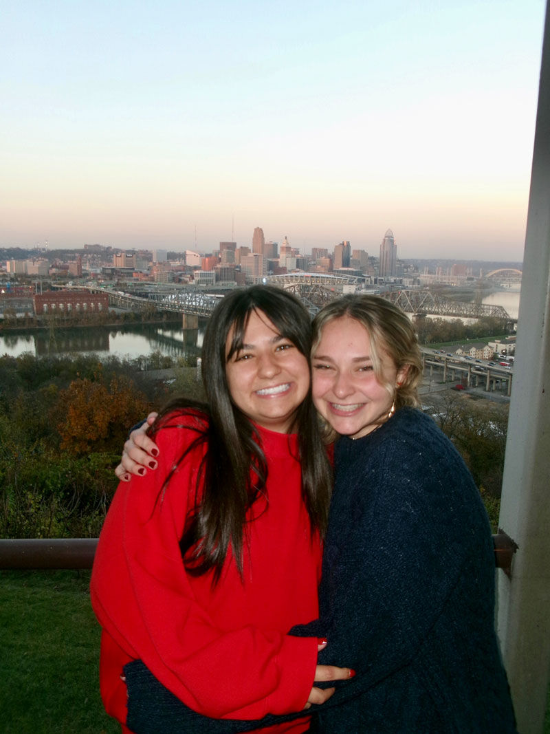 two female friends hugging and smiling in front of Cincinnati skyline