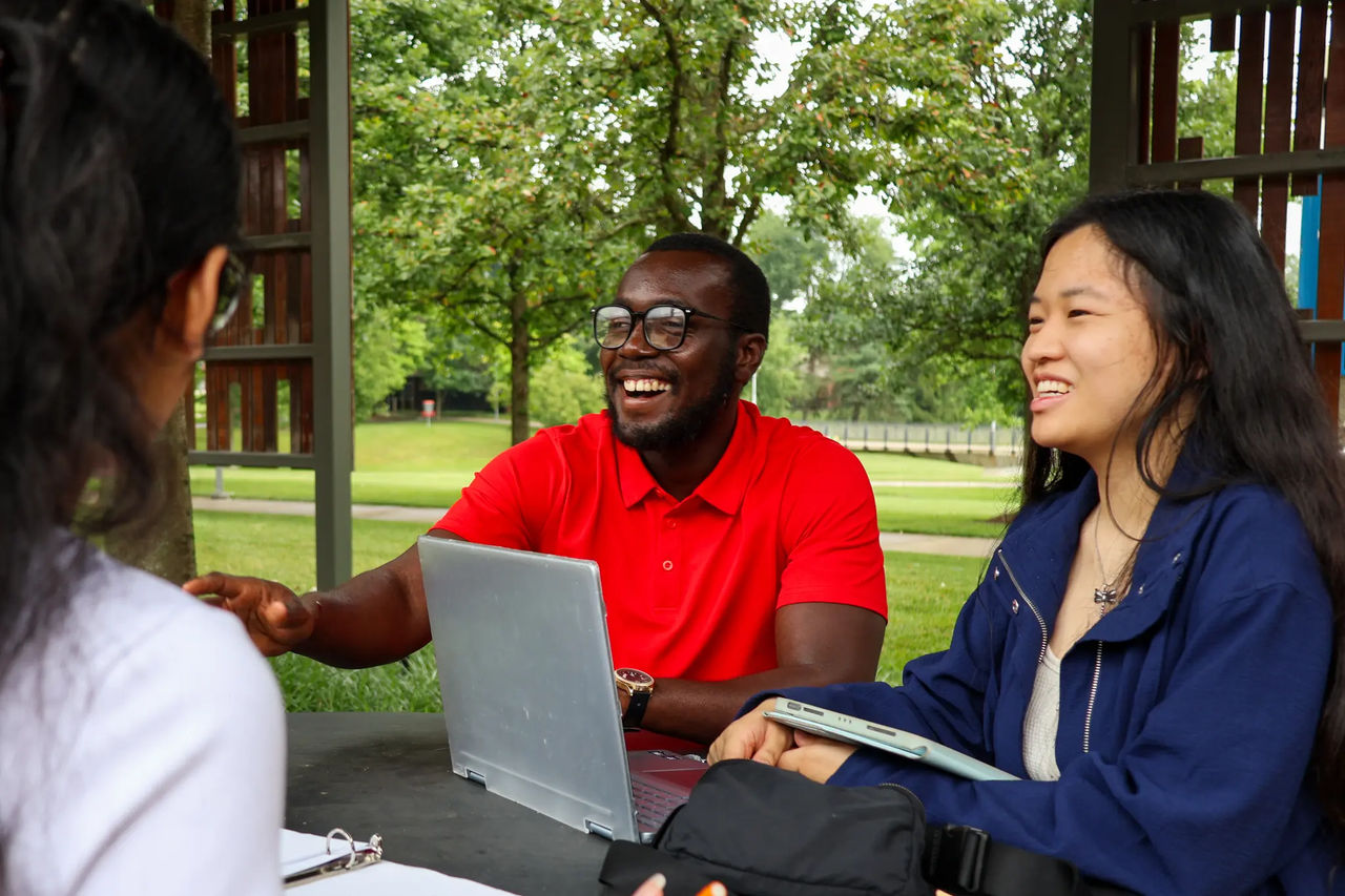 Two students laughing outside with a laptop on the UC Blue Ash patio