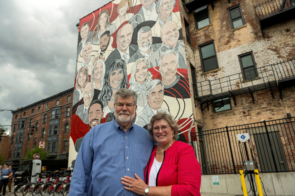 Mark Brueggeman standing with his wife Elizabeth in front of an alumni mural