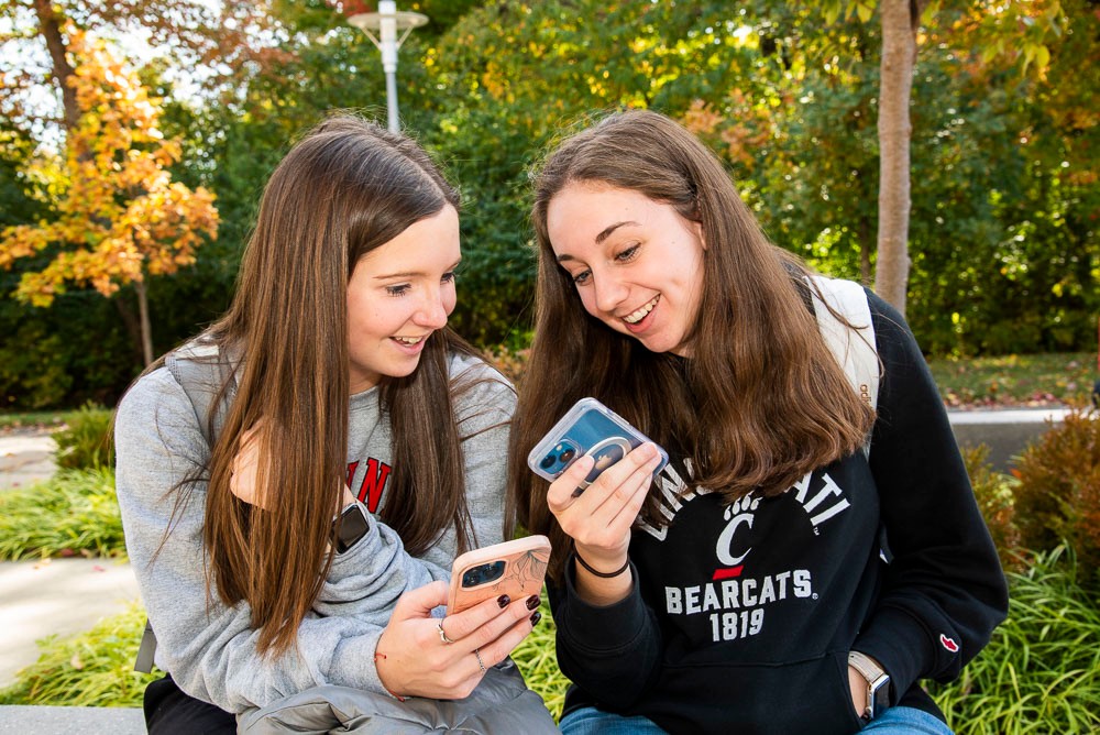 two students laughing outside and looking at phone together