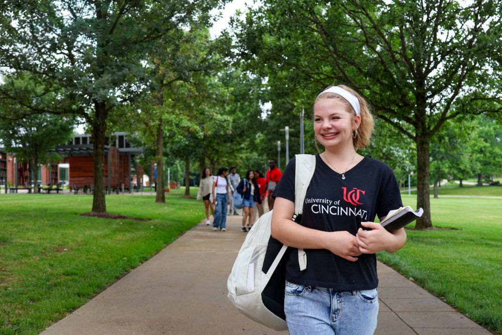 female student walking across wooded UC Blue Ash campus