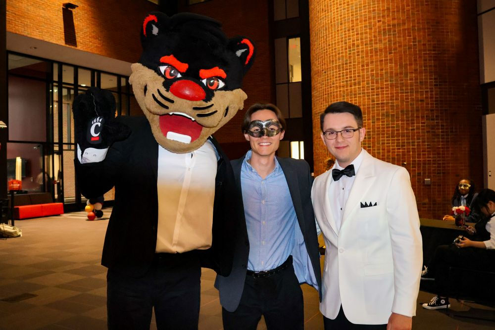 two students in suits posing with the Bearcat mascot