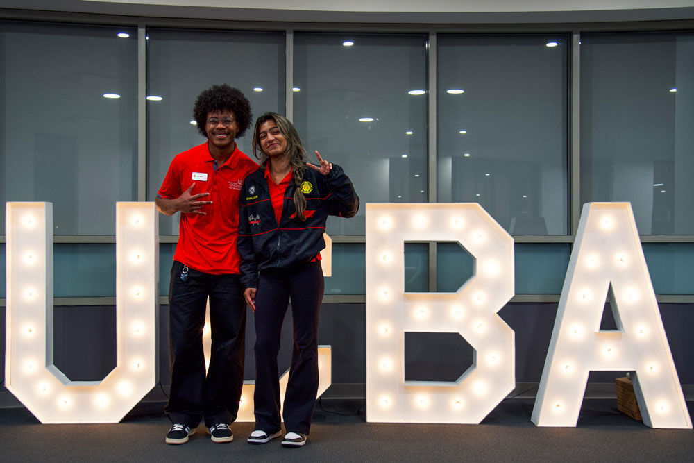 two student posing in front of large UCBA sign