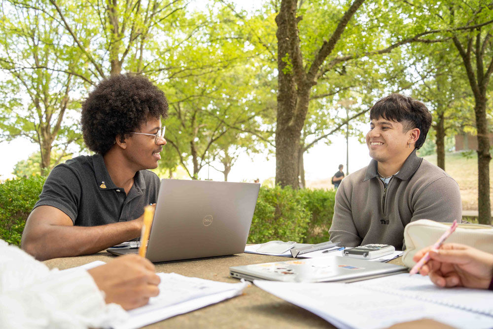 two students sitting outside with laptops at UC Blue Ash College