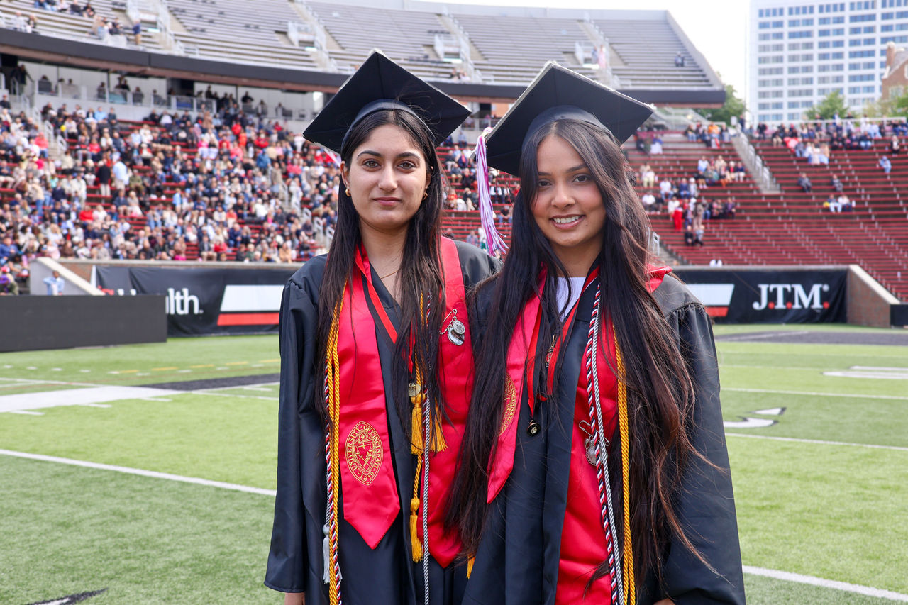 Navpreet  and another student at Nippert Stadium wearing graduation caps and gowns