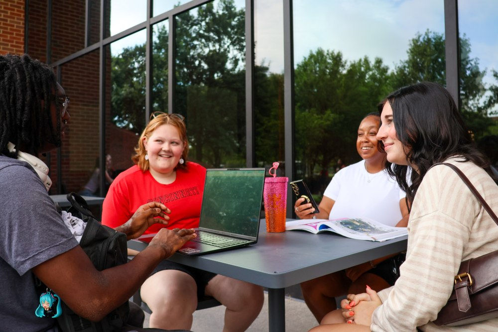 group of students sitting around an outdoor picnic table on the UC Blue ash campus